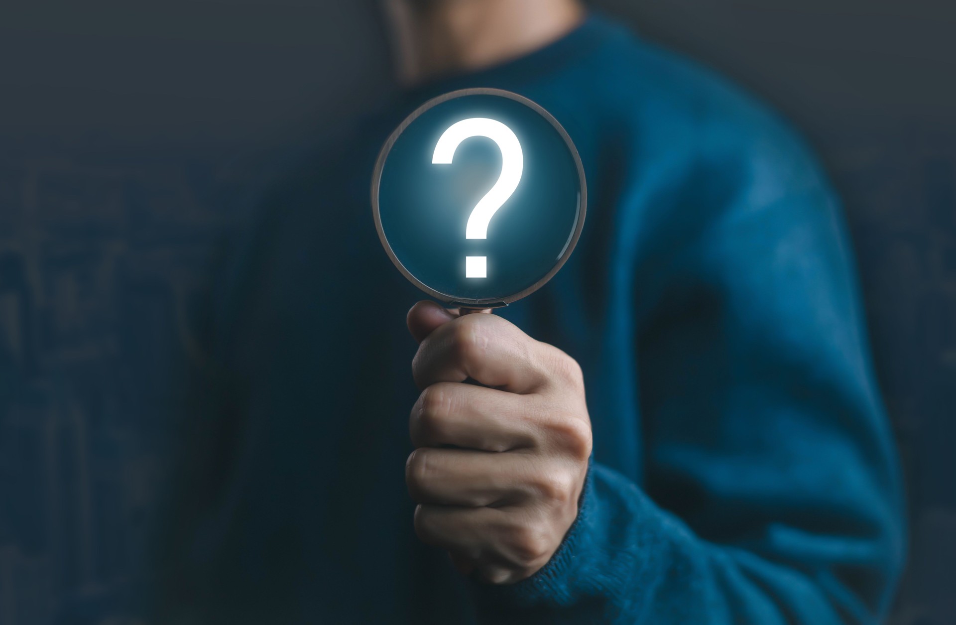 Hand holding magnifying glass with glowing question mark symbol, concept of searching for answers, problem solving, investigation, curiosity, uncertainty, knowledge, and exploration.